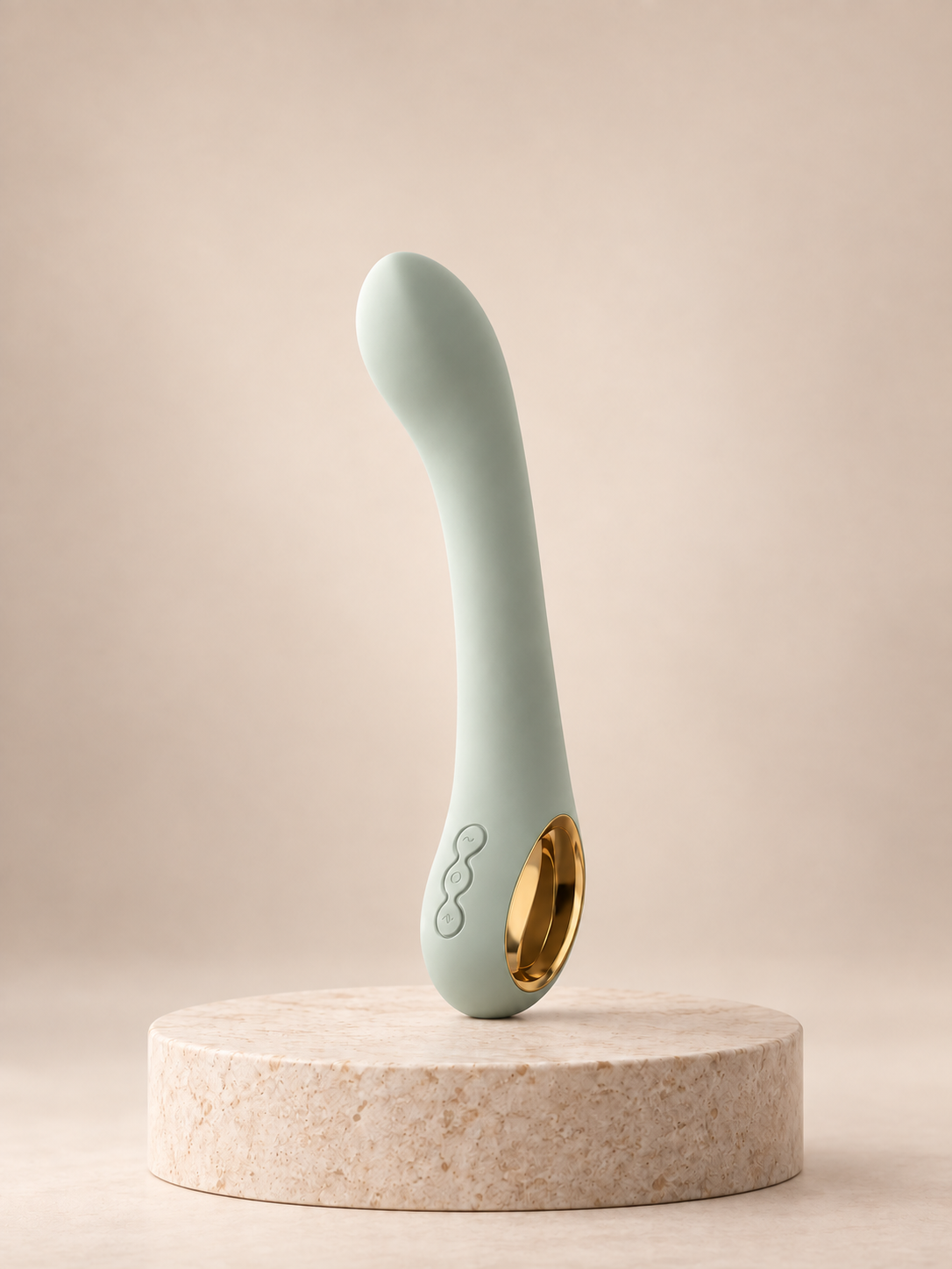 Sage-green vibrator with gold detail on a stone pedestal against a warm neutral background
